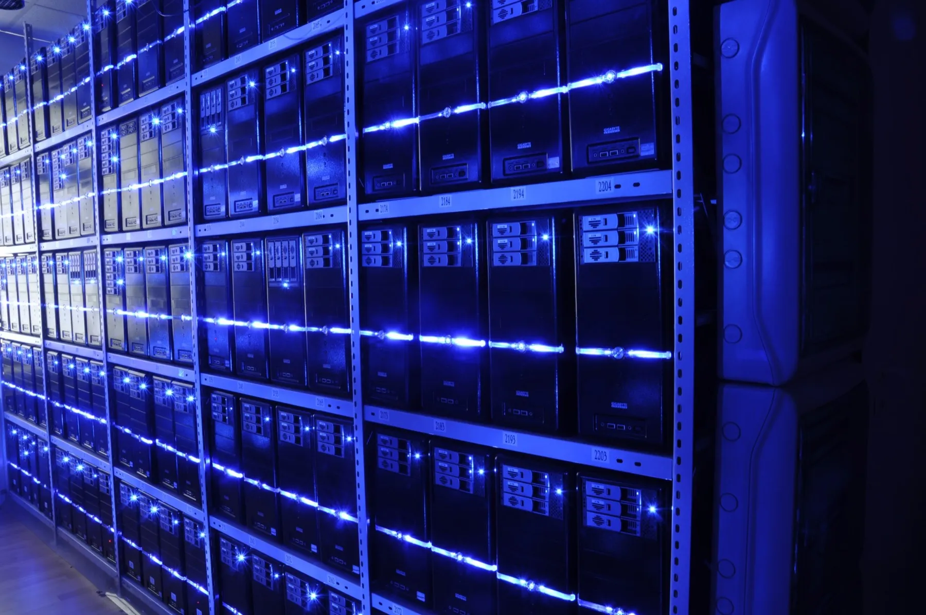 Rows of server racks in a datacentre lit in deep blue, receding into the dark